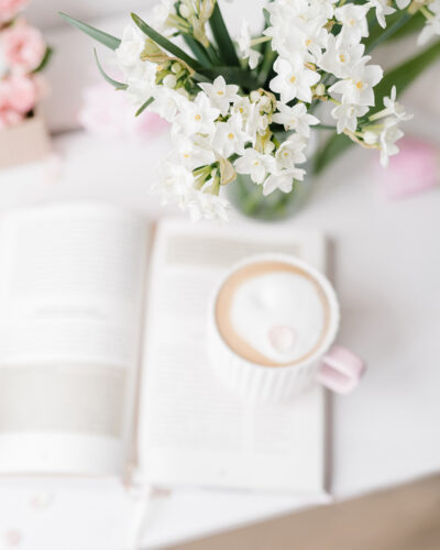 coffee cup and a book with flowers on a white desk space