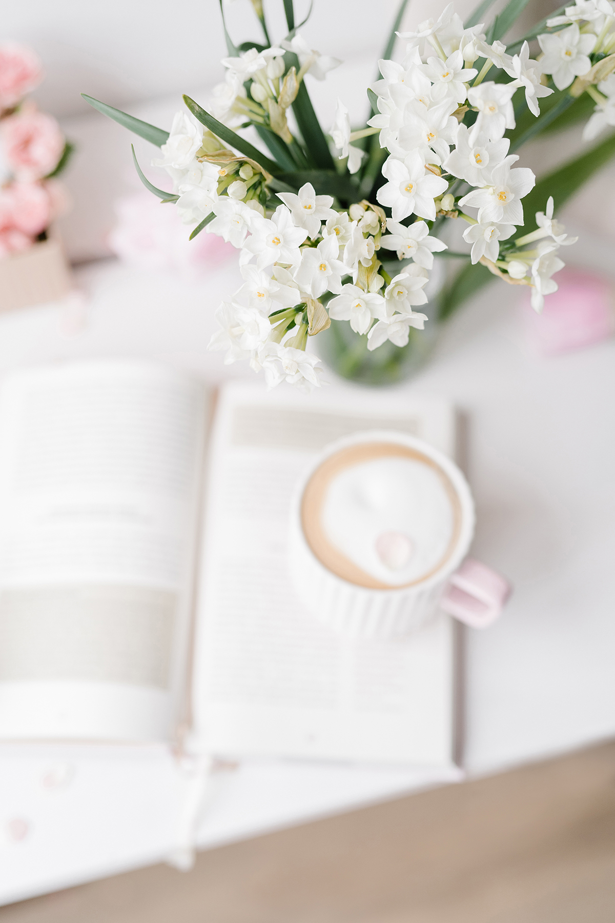 coffee cup and a book with flowers on a white desk space