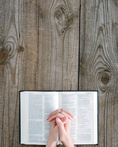 Hands praying over a Bible on a wooden table