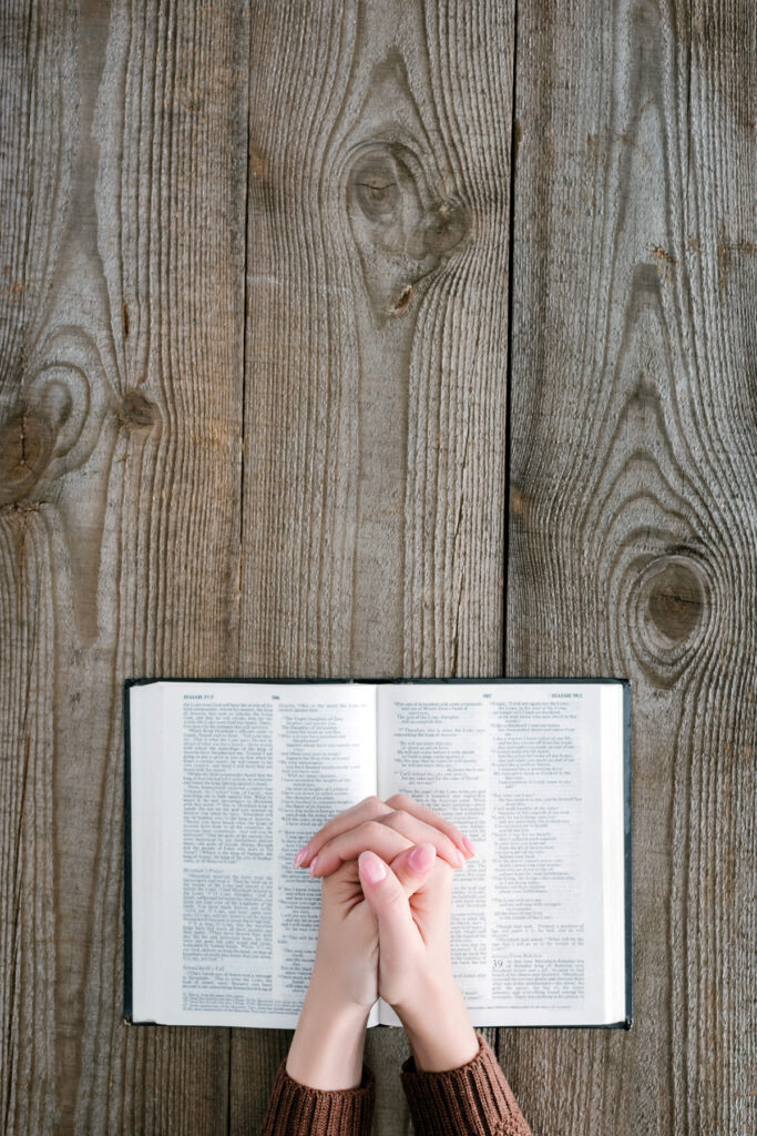 Hands praying over a Bible on a wooden table