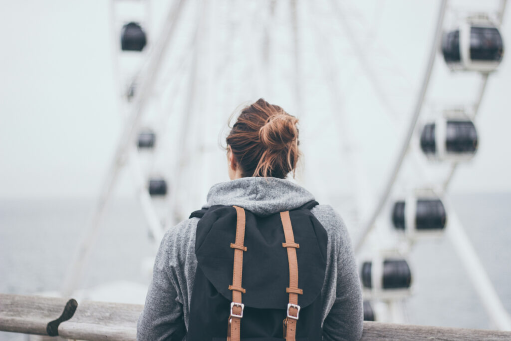 Girl from the back standing with backpack facing a cloudy skyline and ferris wheel